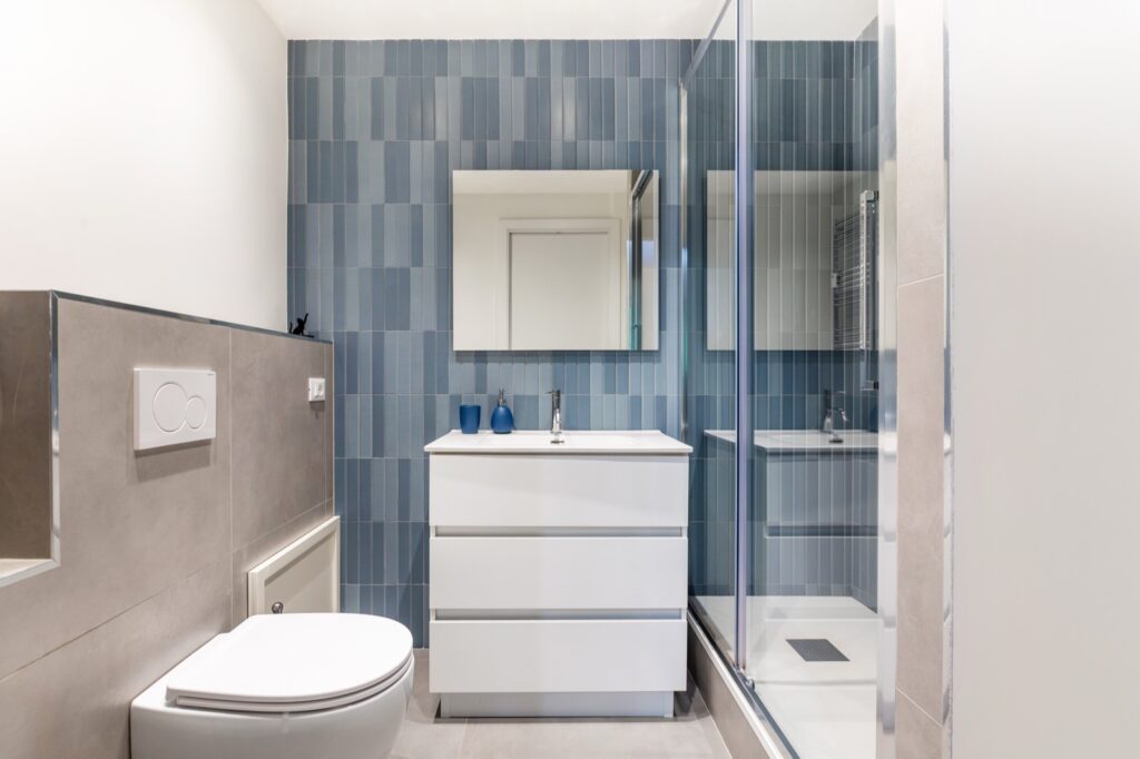 Bagno moderno con piastrelle blu verticali, sanitari sospesi e doccia walk-in in appartamento ristrutturato a Roma — I Ristrutturatori